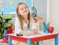 Little blond girl sit at the white desk and laughing in the school classroom