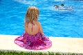 Little blond girl sitting rear back swimming pool