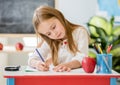 Little blond girl writing classwork in the school classroom