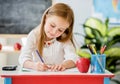 Little blond girl writing classwork in the school classroom