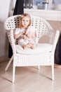 Little blond girl with soft toy sits on large wicker chair