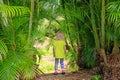 Little blond girl staying among palm trees outdoors