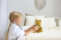 Little blond girl with stethoscope playing with teddy bear