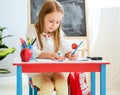 Little blond girl writing classwork in the school classroom