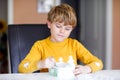 Little blond kid boy with curly hairs eating ice cream at home or in kindergarten. Beautiful child with big icecream box Royalty Free Stock Photo