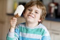 Little blond kid boy with curly hairs eating ice cream popsicle with chocolate at home Royalty Free Stock Photo