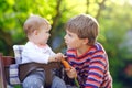 Little blond kid boy giving a carrot to baby sister. Happy siblings eating healthy snack. Baby girl sitting in pram or Royalty Free Stock Photo