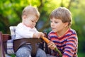 Little blond kid boy giving a carrot to baby sister. Happy siblings eating healthy snack. Baby girl sitting in pram or Royalty Free Stock Photo