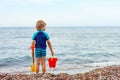 Little blond kid boy standing on lonely ocean beach Royalty Free Stock Photo