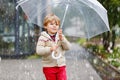 Little blond kid boy walking with big umbrella outdoors on rainy day. Portrait of cute preschool child having fun wear Royalty Free Stock Photo