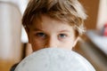 Little blond preschool kid boy with air balloon ball playing indoors at home or nursery. Funny child having fun alone Royalty Free Stock Photo