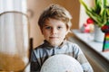 Little blond preschool kid boy with air balloon ball playing indoors at home or nursery. Funny child having fun alone Royalty Free Stock Photo