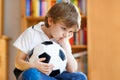 Sad and not happy little kid with football about lost football or soccer game. child after watching match on tv