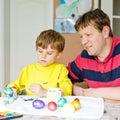 Little blond preschool kid boy and father coloring eggs for Easter holiday in domestic kitchen, indoors. Child and dad Royalty Free Stock Photo