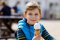Little blond school kid boy with curly hairs eating ice cream cone, with waffle outdoors on warm sunny day. Happy Royalty Free Stock Photo