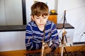 Little blond school kid boy playing with sailing ship model indoors. Excited child with yacht having fun after school at Royalty Free Stock Photo