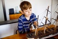 Little blond school kid boy playing with sailing ship model indoors. Excited child with yacht having fun after school at Royalty Free Stock Photo