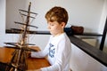 Little blond school kid boy playing with sailing ship model indoors. Excited child with yacht having fun after school at Royalty Free Stock Photo