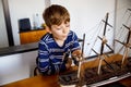 Little blond school kid boy playing with sailing ship model indoors. Excited child with yacht having fun after school at Royalty Free Stock Photo