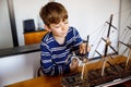 Little blond school kid boy playing with sailing ship model indoors. Excited child with yacht having fun after school at Royalty Free Stock Photo