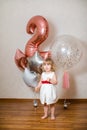 Little blonde baby girl two years old with big pink and white balloons on her birthday party Royalty Free Stock Photo