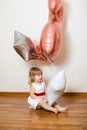 Little blonde baby girl two years old with big pink and white balloons on her birthday party