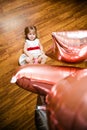 Little blonde baby girl two years old with big pink and white balloons lying on the wooden floor on her birthday party Royalty Free Stock Photo