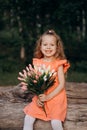 A little blonde with a bouquet in her hand looks at the camera and smiles beautifully