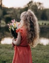 A little blonde with a bouquet in her hand looks into the distance with her back to the camera