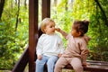 A little blonde boy and an African-American girl in a park on a bench eating a bar of white and dark chocolate Royalty Free Stock Photo