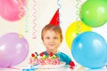 Little blonde boy in festive hat with birthday cake and balloons Royalty Free Stock Photo