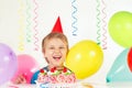 Little blonde boy in holiday hat with birthday cake and balloons Royalty Free Stock Photo