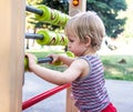 Little blonde boy in striped shirt moves round green cubes on the playground in the park