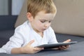 Little blonde boy using touchscreen tablet at home. Happy smart child watching tutorials or playing game on tablet computer.