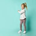 Little blonde child in shirt with hearts print, checkered pants, white sneakers. Smiling, posing on blue background. Full length Royalty Free Stock Photo