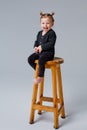 A little blonde girl with blue eyes in black clothes sits on a high chair in the studio on a solid gray background Royalty Free Stock Photo