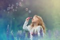 Little blonde girl with curly hair walking in a field with lupins, blowing soap bubbles, summer evening Royalty Free Stock Photo