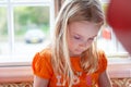 Little blonde girl dressed vibrantly in orange, looking down concentrating