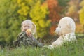 Little blonde girl eats apple and plays with large teddy bear sitting on grass. Child on walk on autumn day in nature Royalty Free Stock Photo