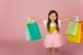 Little blonde girl enjoys her shopping on a pastel pink background with copyspace. Sale. Cute little girl with many multicolored