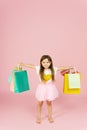 Little blonde girl enjoys her shopping on a pastel pink background with copyspace. Sale. Cute little girl with many multicolored