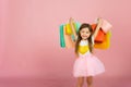 Little blonde girl enjoys her shopping on a pastel pink background with copyspace. Sale. Cute little girl with many