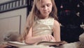 A little blonde girl in a festive dress with a book in her hands sits next to soft toys against the background of a Royalty Free Stock Photo