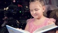 A little blonde girl in a festive dress with a book in her hands sits next to soft toys against the background of a Royalty Free Stock Photo