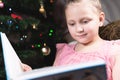 A little blonde girl in a festive dress with a book in her hands sits next to soft toys against the background of a Royalty Free Stock Photo