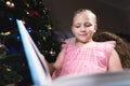 A little blonde girl in a festive dress with a book in her hands sits next to soft toys against the background of a Royalty Free Stock Photo