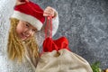 Little blonde girl in a gnomes red hat opening santa`s bag in anticipation of a Christmas miracle Royalty Free Stock Photo