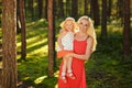 Little blonde girl and her mom smiling in the forest in sunny summer.