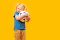 Little blonde girl holding soccer ball on yellow studio background. Copy space, mockup. Football for kids concept Royalty Free Stock Photo