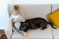 a little blonde girl at home on the sofa with a mobile phone and a big dog, children and gadgets